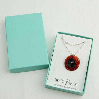 Spiral of red and black glass to replicate a poppy flower on a silver chain in a turquoise gift box