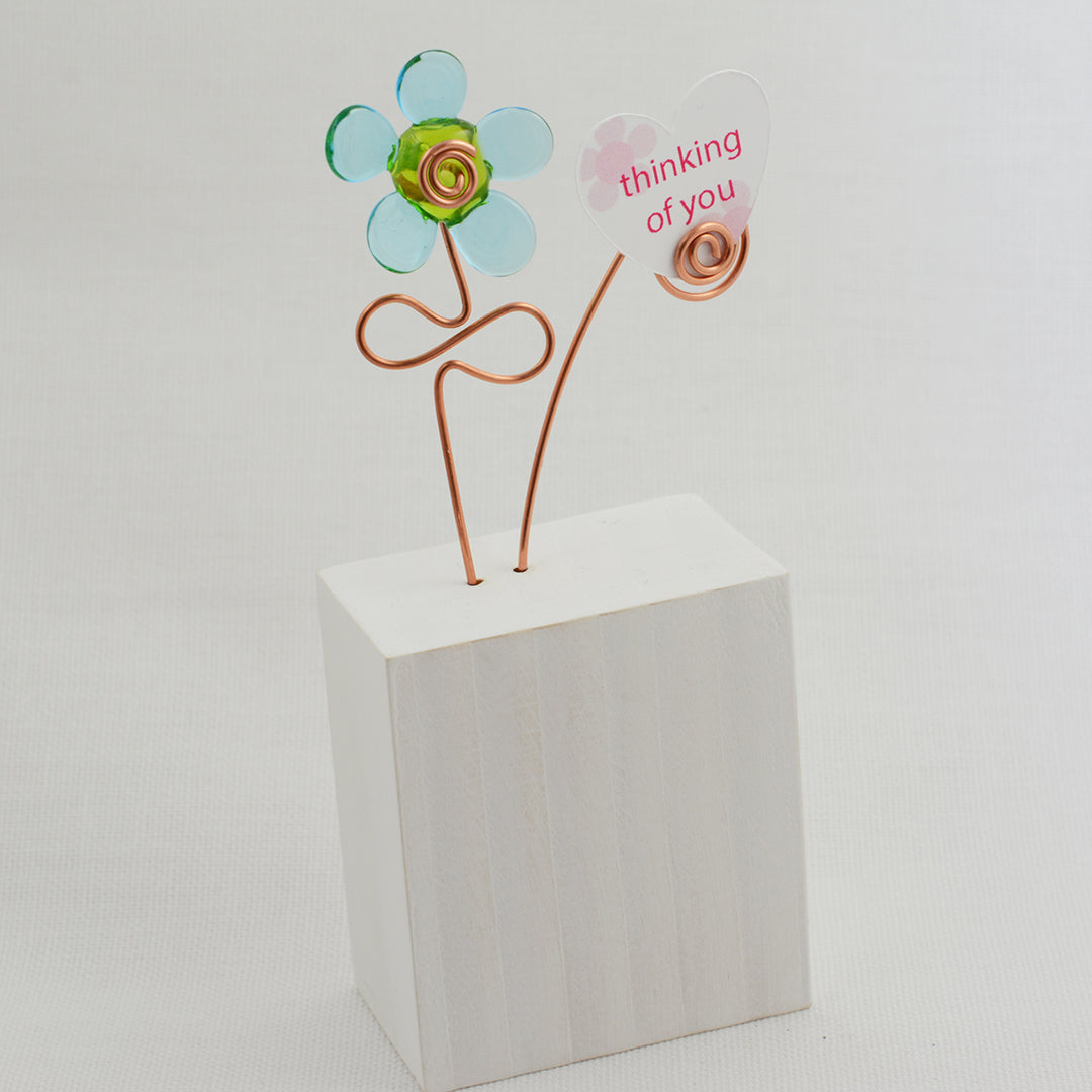 Turquoise and green glass flower on a white wooden block with a paper heart with the message 'Thinking of You'